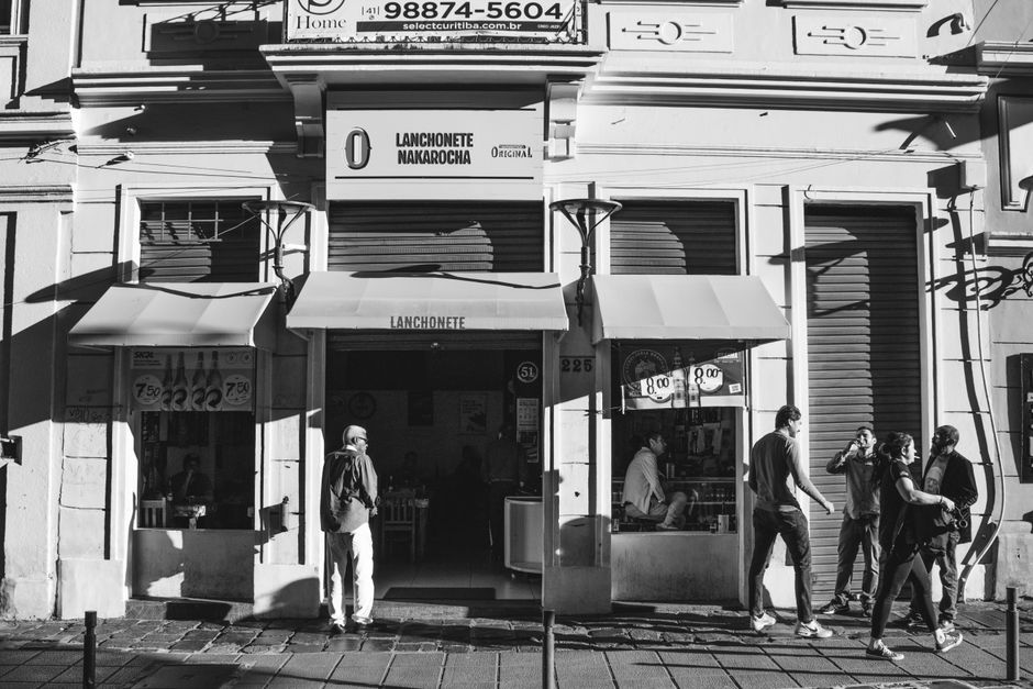 Imagem monocromática de pedestres fora de um café em uma movimentada rua urbana.